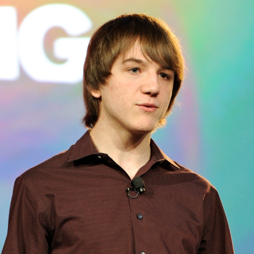 Teen inventor Jack Andraka speaking on stage in a light gray blazer against a blue backdrop, hands gesturing passionately.